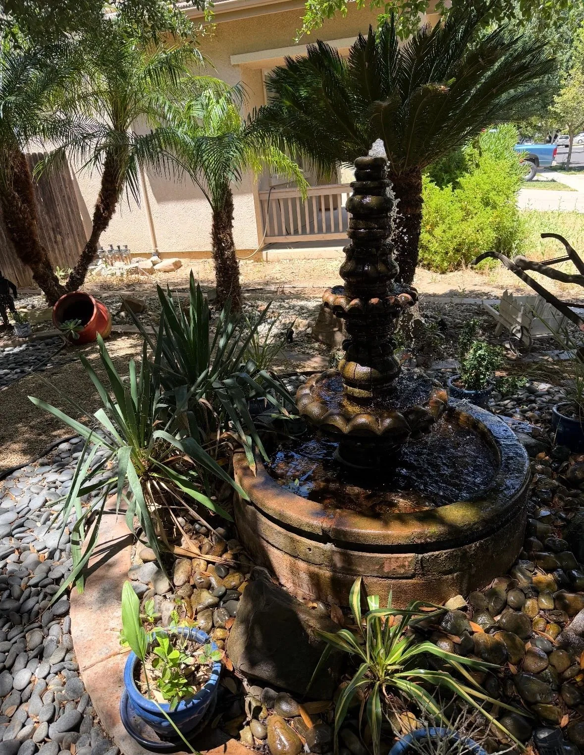 Backyard garden with a stone fountain, potted plants, and layered beds