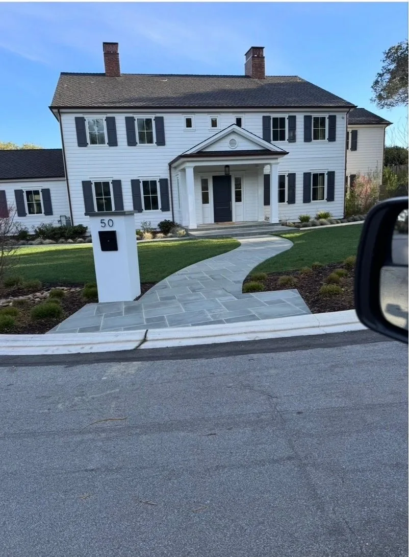 Curved bluestone walkway leading to a white house with a modern mailbox pillar