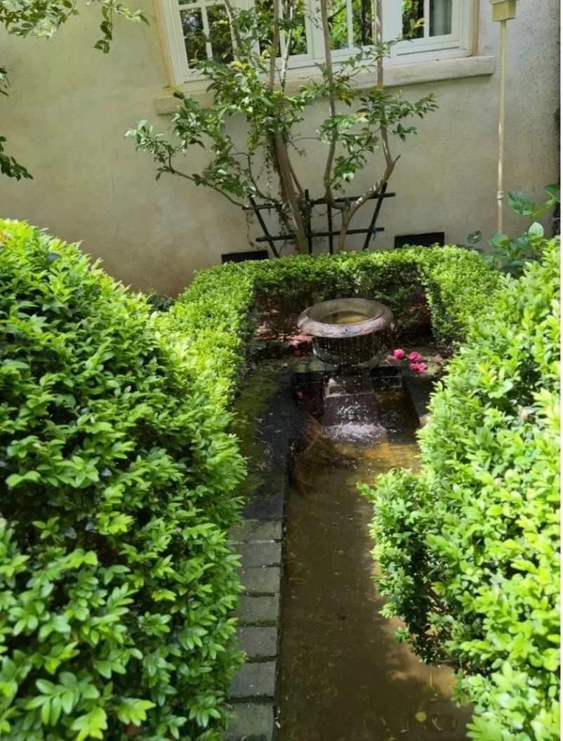 Formal stone water rill with a central urn framed by clipped boxwood hedges