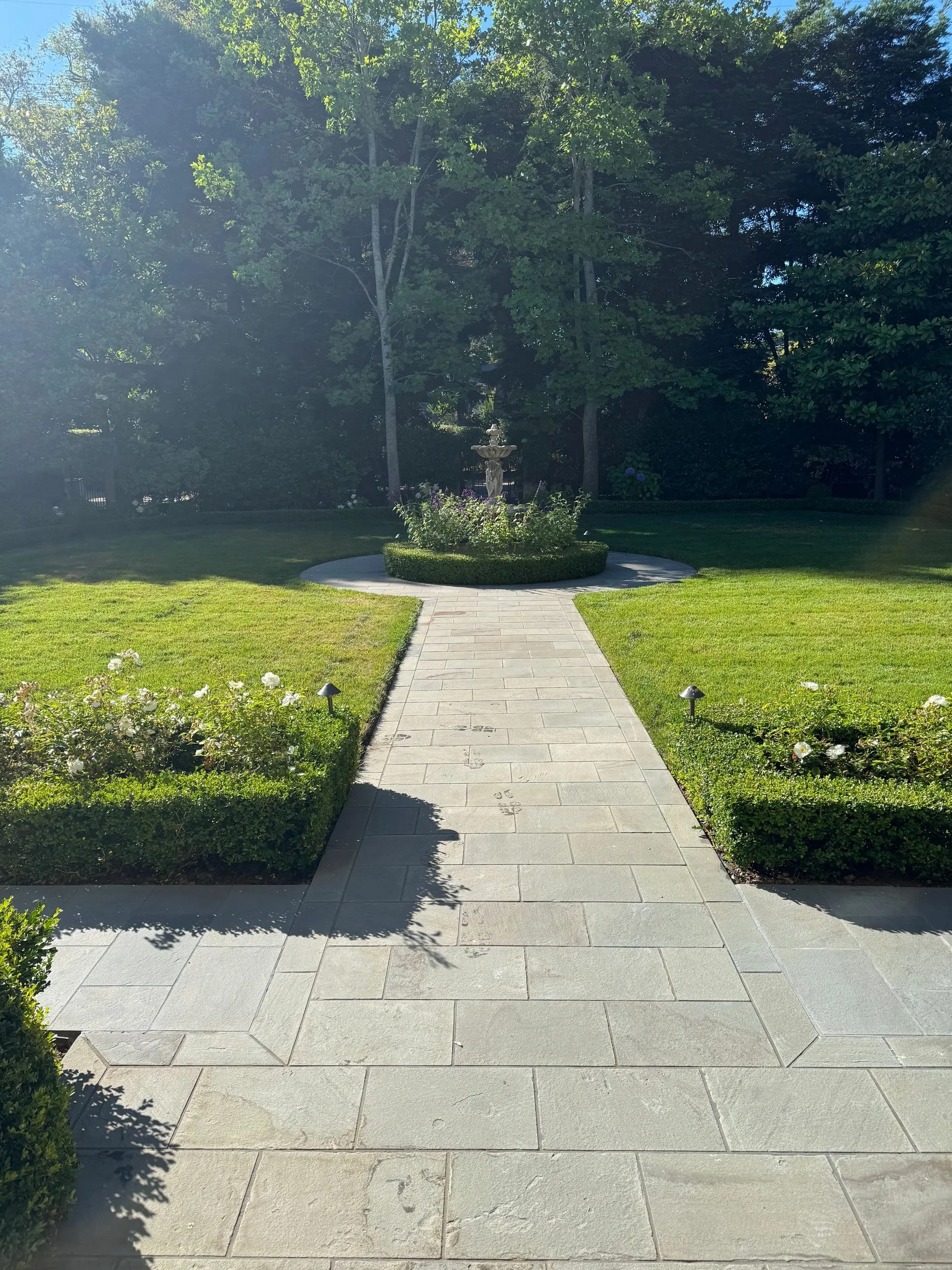 Straight stone walkway crossing a lawn toward a circular planting bed
