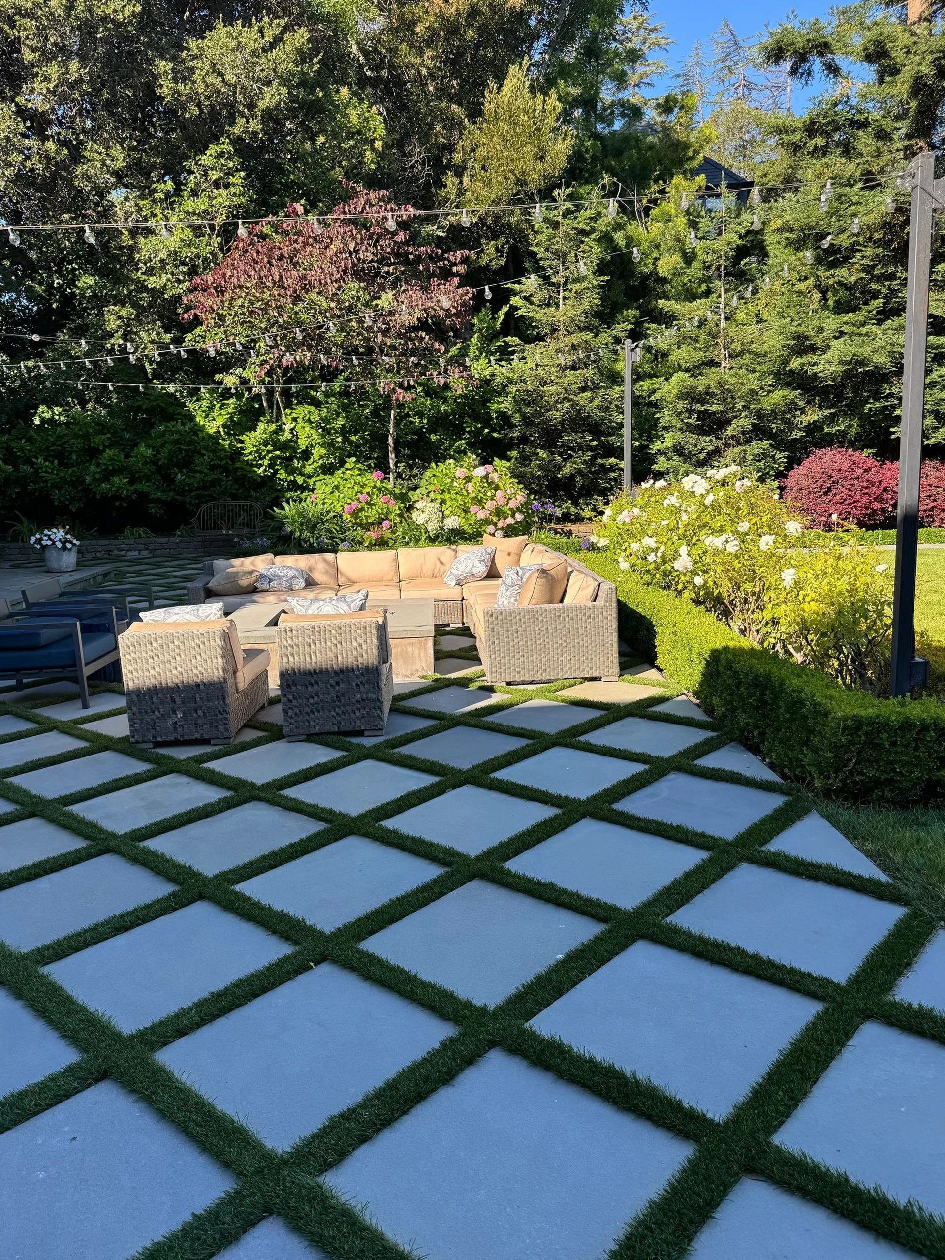 Patio seating area surrounded by clipped hedges and lawn-grid paving