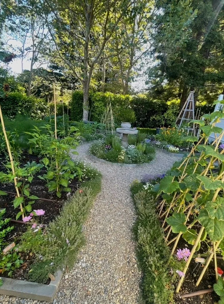 Pea-gravel paths through a vegetable garden with trellises and a stone birdbath