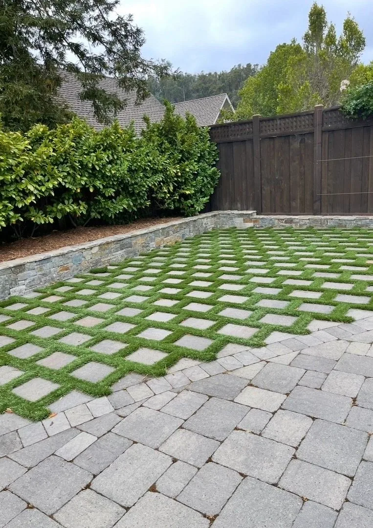 Grid of pale concrete pavers and grass meeting a paved driveway