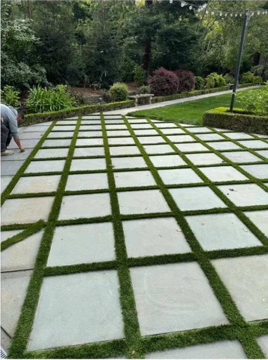 Square paver grid with grass strips being installed on a backyard patio
