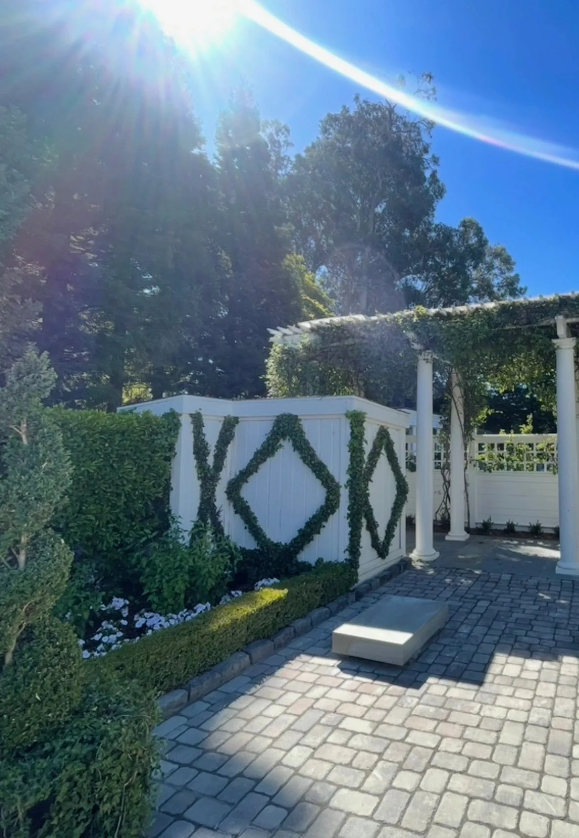 Cobblestone patio beside a white pergola and ivy diamond trellis wall