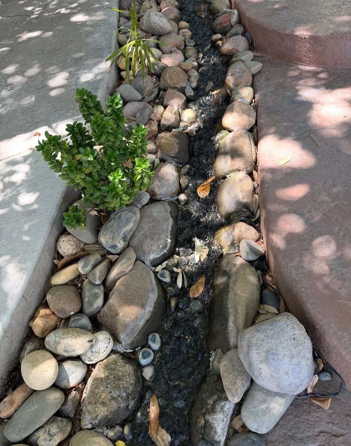 Narrow rocky stream with flowing water between concrete walkways