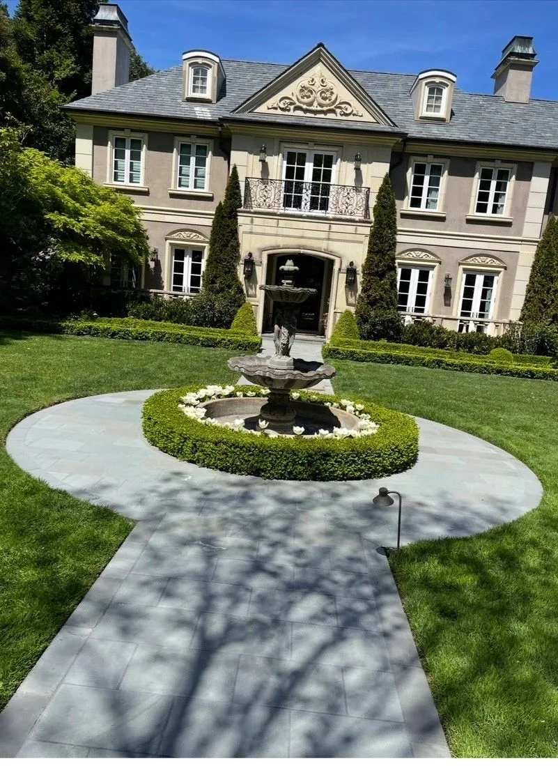Three-tiered stone fountain on a circular flagstone patio beside a formal lawn