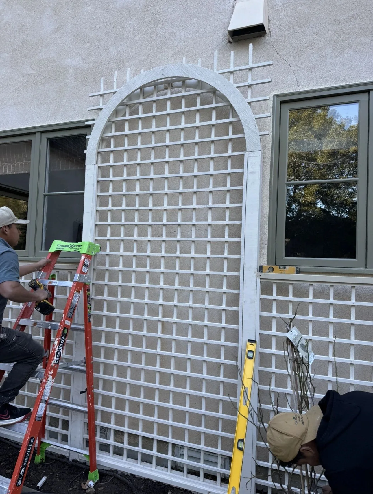 White arched garden trellis installed against a light exterior wall